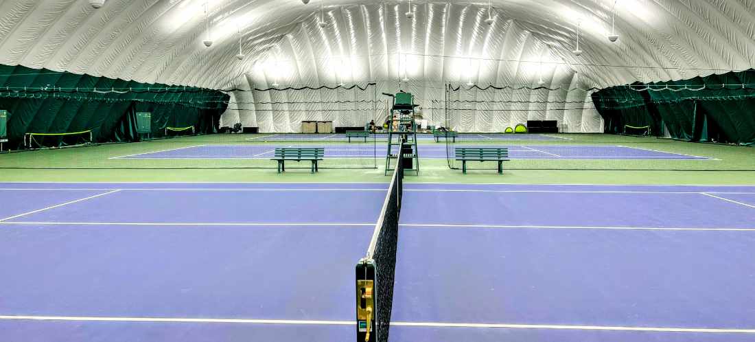 People play tennis on 3 courts inside a green and white indoor dome